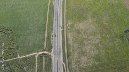 Top-down aerial view of an asphalt road passing through green fields.