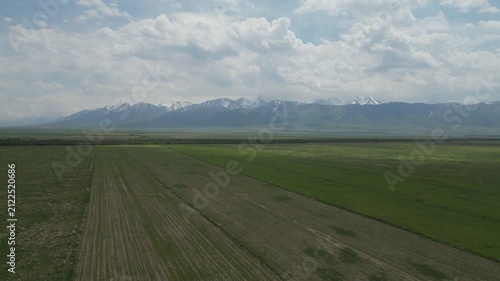 Wide shot of open farmland with snow-capped mountains in the background.