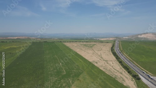 Aerial view of a long highway cutting through green fields and hills.