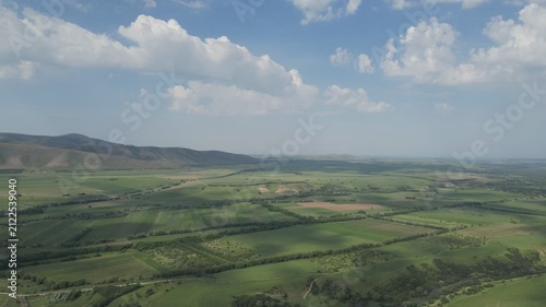 Aerial view of green agricultural fields and hills under a cloudy sky.