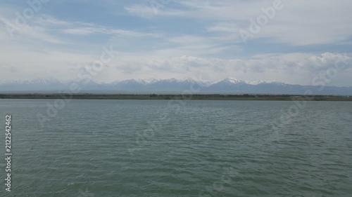 Scenic lake view with snow-capped distant mountains under a cloudy sky.