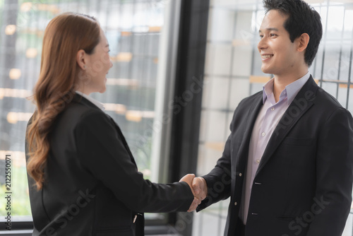 Close up of smiling Asian businessman and businesswoman shaking hands in corporate office.