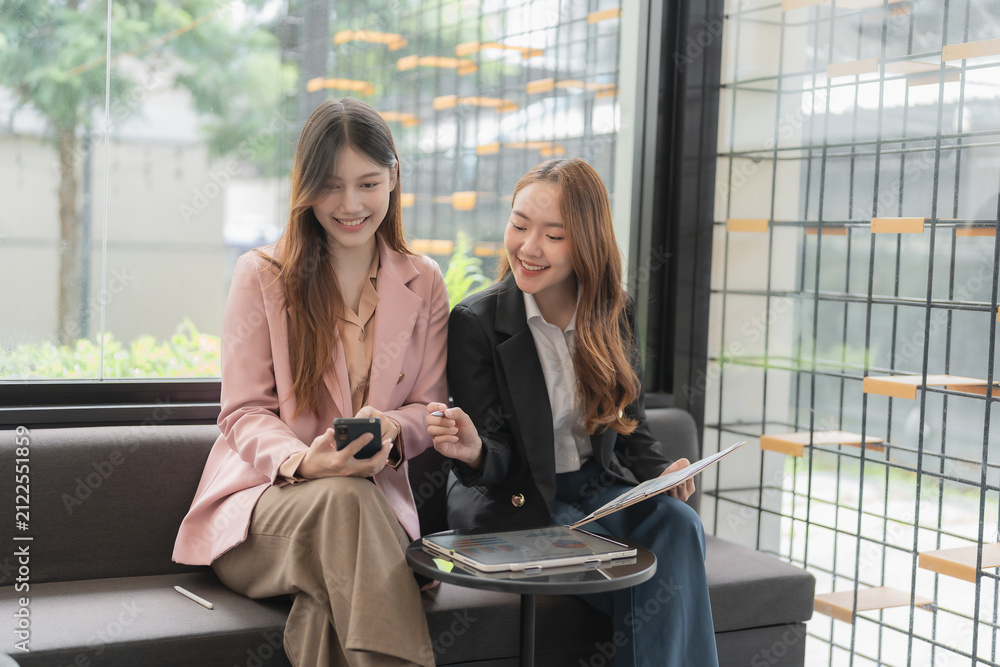 Fototapeta premium Two happy Asian businesswomen working together with tablet and smartphone in office.