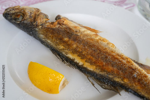 Konstfotografi A whole grilled fish served on a white plate with a lemon wedge.