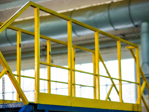 Obraz na płótnie Bright yellow metal safety guard rails line an elevated industrial platform walkway inside a manufacturing plant facility