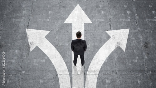 Businessman standing at crossroads with arrows on pavement choosing direction and career path