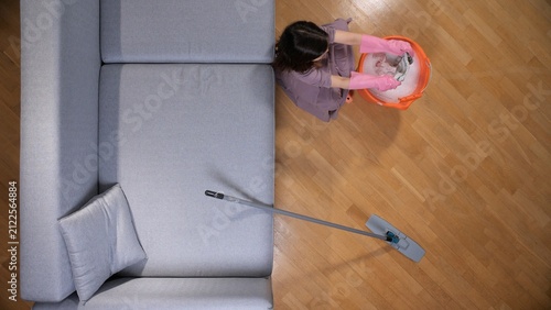 Cuadro en lienzo Woman in pink gloves preparing a mop in a bucket with soapy water, standing on a