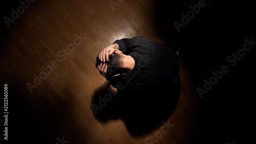 Cuadro en lienzo Depressed man with head in hands sitting alone on a wooden floor in a dark room,