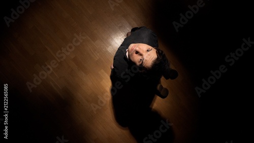 Foto Man standing on a wooden floor in a dark room, looking up towards a bright light