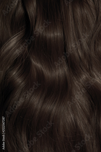 Brown hair close-up as a background. Women's long brown hair. Beautifully styled wavy shiny curls. Hair coloring. Hairdressing procedures, extension.