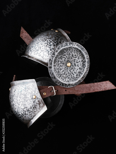 Hammered steel shoulder cops with textured surfaces, brass rivets, rondel discs, and leather straps, photographed on dark background.