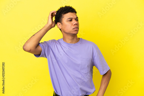 Canvas Print Young African American man isolated on yellow background having doubts while scr