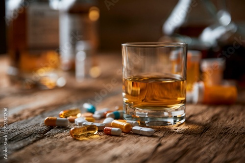 Glass of whiskey on a wooden table with scattered pills and bottles in the background