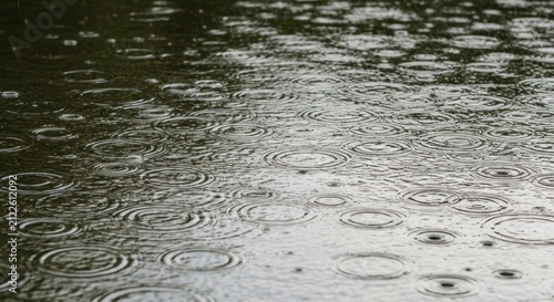 Still water surface reflecting the sky, pocked with raindrops creating circular ripples