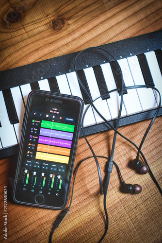 Smartphone with music app and headphones on keyboard against wooden background