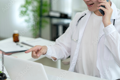 Male Doctor Consulting Patient by Phone While Reviewing Laptop in Modern Medical Office