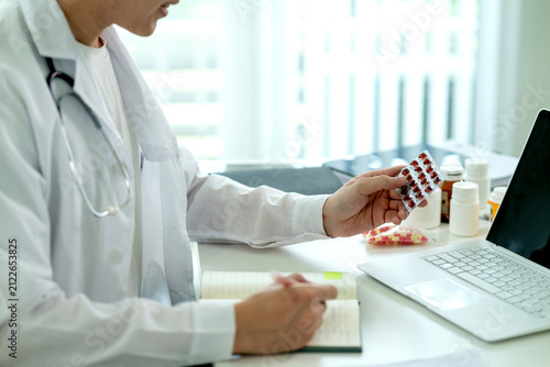 Male Doctor Reviewing Patient Medication Information at Modern Medical Office Desk with Laptop