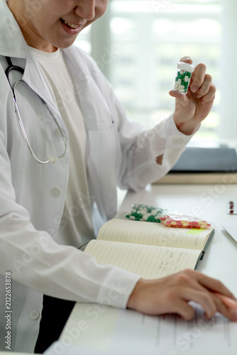 Male Doctor Examining Medication Capsules While Consulting Medical Notebook in Modern Clinic