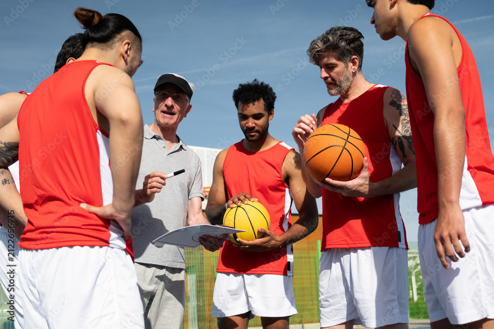 Fototapeta premium Basketball coach discussing strategy with his multi ethnic team during an outdoor practice