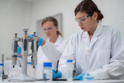 Canvastavla Professional female scientist writing research data on digital tablet in modern laboratory with colleague