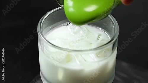 Barista mixing matcha green tea powder and pouring creamy matcha foam over iced milk in glass