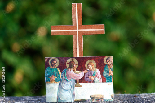 A religious still life featuring a handmade cross and a religious image depicting Jesus distributing the Eucharist.