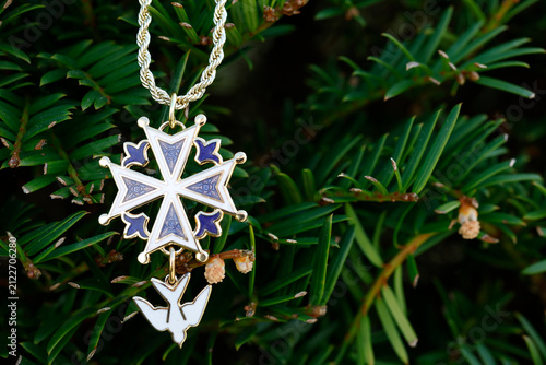 Fotografie A Huguenot cross hanging from a conifer branch in a natural outdoor setting