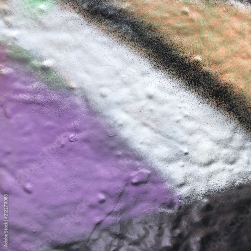 Abstract purple, white, black and beige graffiti spray paint texture on bumpy wall surface