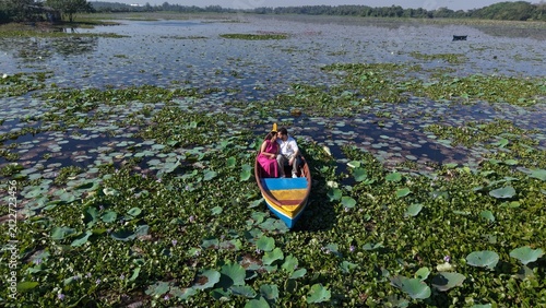Quadro su tela Aerial drone view of a couple enjoying a colorful boat ride across a scenic lake covered with lotus leaves and aquatic plants, surrounded by lush greenery