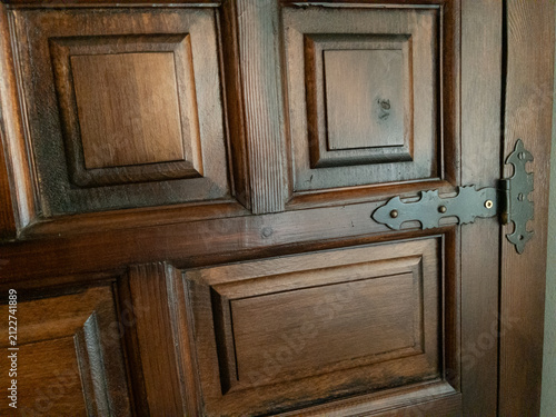 Dark wooden door featuring antique hinge and carved panels