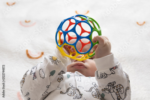 Close-up of an infant lying on a soft blanket while holding a colorful sensory ball.