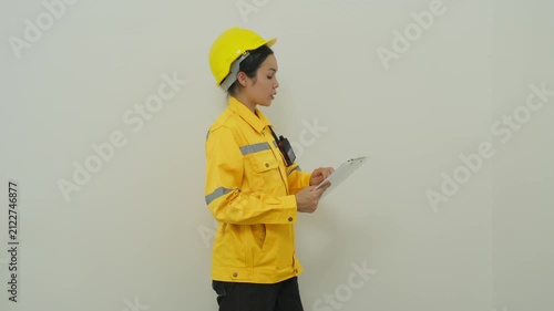 Home inspector in yellow helmet and jacket examining interior wall with clipboard, focused professional profile, surveying wall in safety jacket and helmet