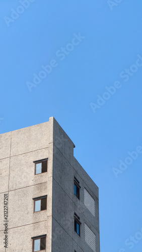 Minimalist concrete building corner against clear blue sky. A sharp vertical perspective of a modern textured concrete building corner on cloudless blue sky, showcasing minimalist urban architecture.