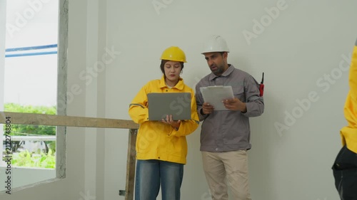 Construction worker and engineer discussing plan indoors near unfinished wall with laptop and document, home inspector checking building interior with clipboard and laptop, home inspector discussing