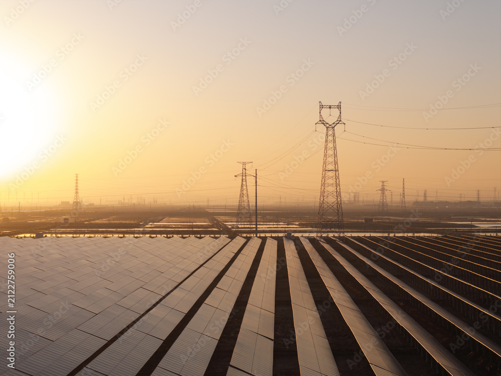 Naklejka premium Solar power station and transmission towers at sunrise with orderly photovoltaic arrays and metallic structures