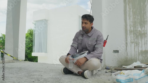 Home inspector construction site checking wall and floor surface, sitting concrete with tool and notebook, drinking water during building inspection near unfinished wall, seated floor with sample