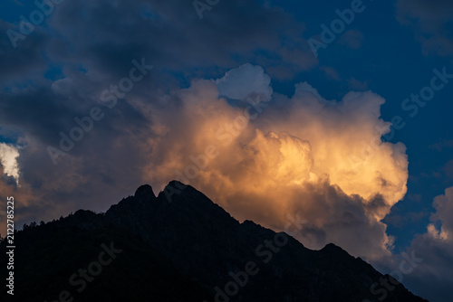 Dramatic sky with clouds and silhouette of a mountain peak at sunset in summer