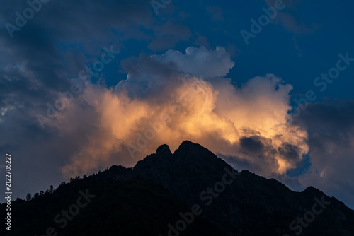 Dramatic sky with clouds and silhouette of a mountain peak at sunset in summer