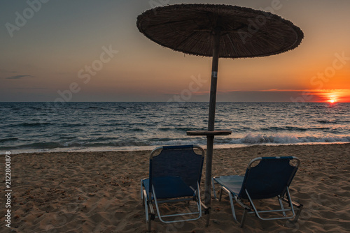 Obraz na plátně Empty beach chairs under parasol at sunset on the Greek coast