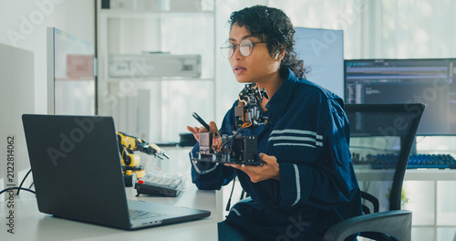 Young African American female robotics engineer discussing mechanical part on video call in laboratory. Remote work, virtual training, online meeting, future technology, technical support concept.