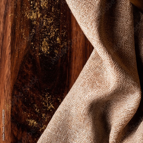 Dark walnut wood grain meets a fold of natural linen fabric with brass flecks, creating a warm tactile backdrop for hospitality and barware design