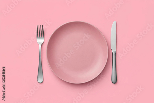 Dinner place setting. A pink plate with silver fork and knife isolated on pink background with clipping path
