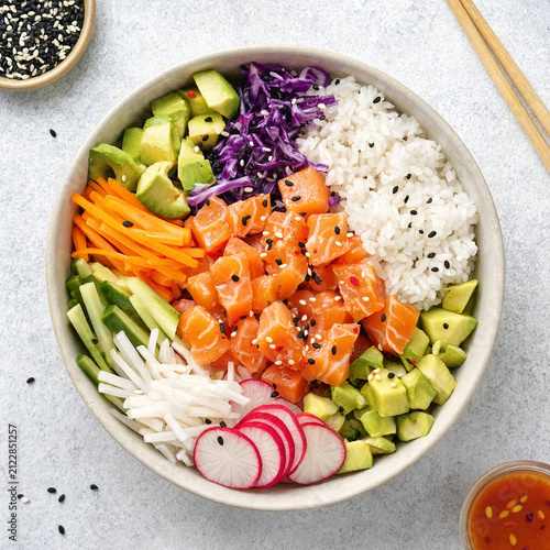 Fresh salmon poke bowl with rice, avocado, cucumber, radish and cabbage in a top down flatlay