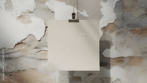Square paper sheet hanging with a metal clip on a textured rustic wall, interior mockup