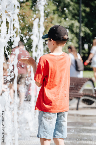 Boy playing with splashing water at an outdoor city fountain during a sunny summer day, active childhood recreation