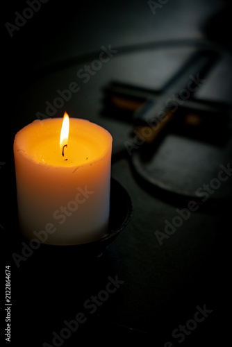 Burning candle with blurred Christian cross in a dark church interior