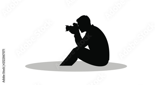 Fotografie A silhouetted photographer is kneeling while intently focused on a subject throu