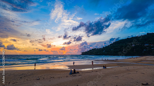 Aerial style timelapse view of a dramatic sunset, the sky transforms into rich hues of gold, red, and purple above the sea and distant island.