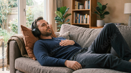 Man relaxing on sofa listening to music with headphones at home