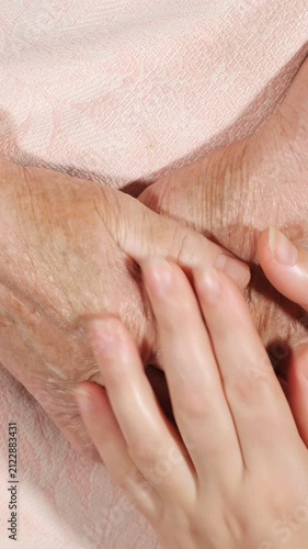 Close up view of a young caregiver tenderly massaging the aged, wrinkled hands of an elderly woman, symbolizing intergenerational support, love, and assistance for seniors